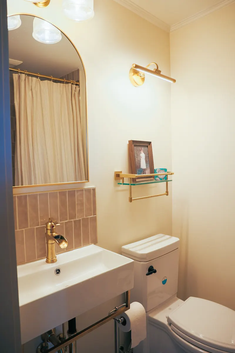 The hallway bathroom — a wall-hung basin with a brass tap under an arched mirror and a picture light.
