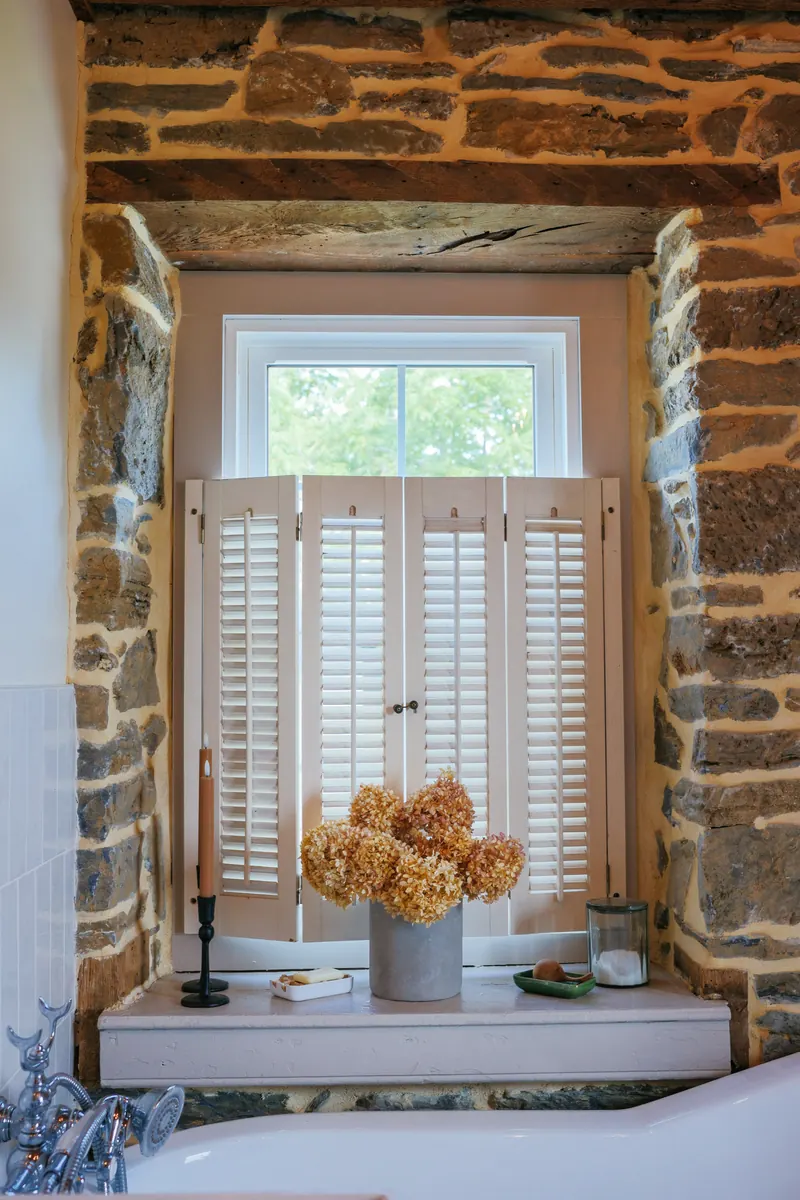 A deep stone window reveal in the Paris ensuite, louvered shutters and a zinc pot of dried hydrangeas on the sill.