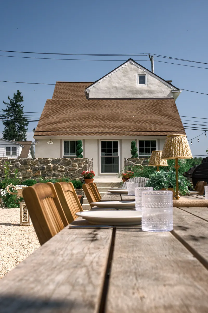 The outdoor table set with plates and cut glass, the house and its stone wall behind.