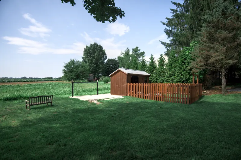 The garden shed behind a picket fence at the edge of the lawn, a bench facing the open field.