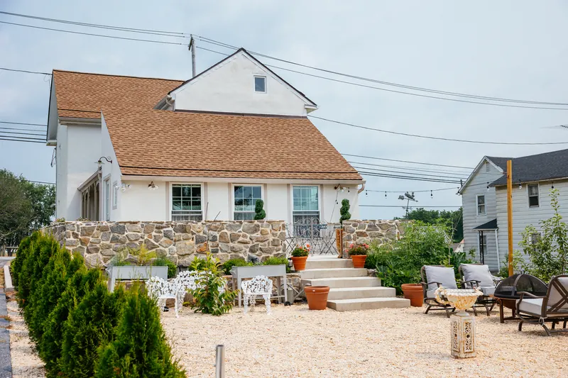 The house from the gravel terrace — a stone retaining wall, clipped box in terracotta pots, and steps up to the door.