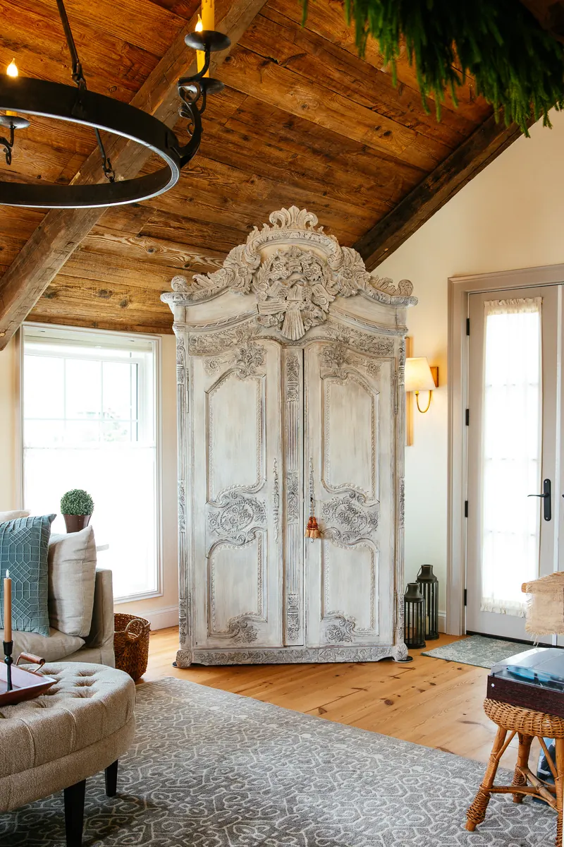 A carved limewashed French armoire in the living room, beneath a beamed ceiling.