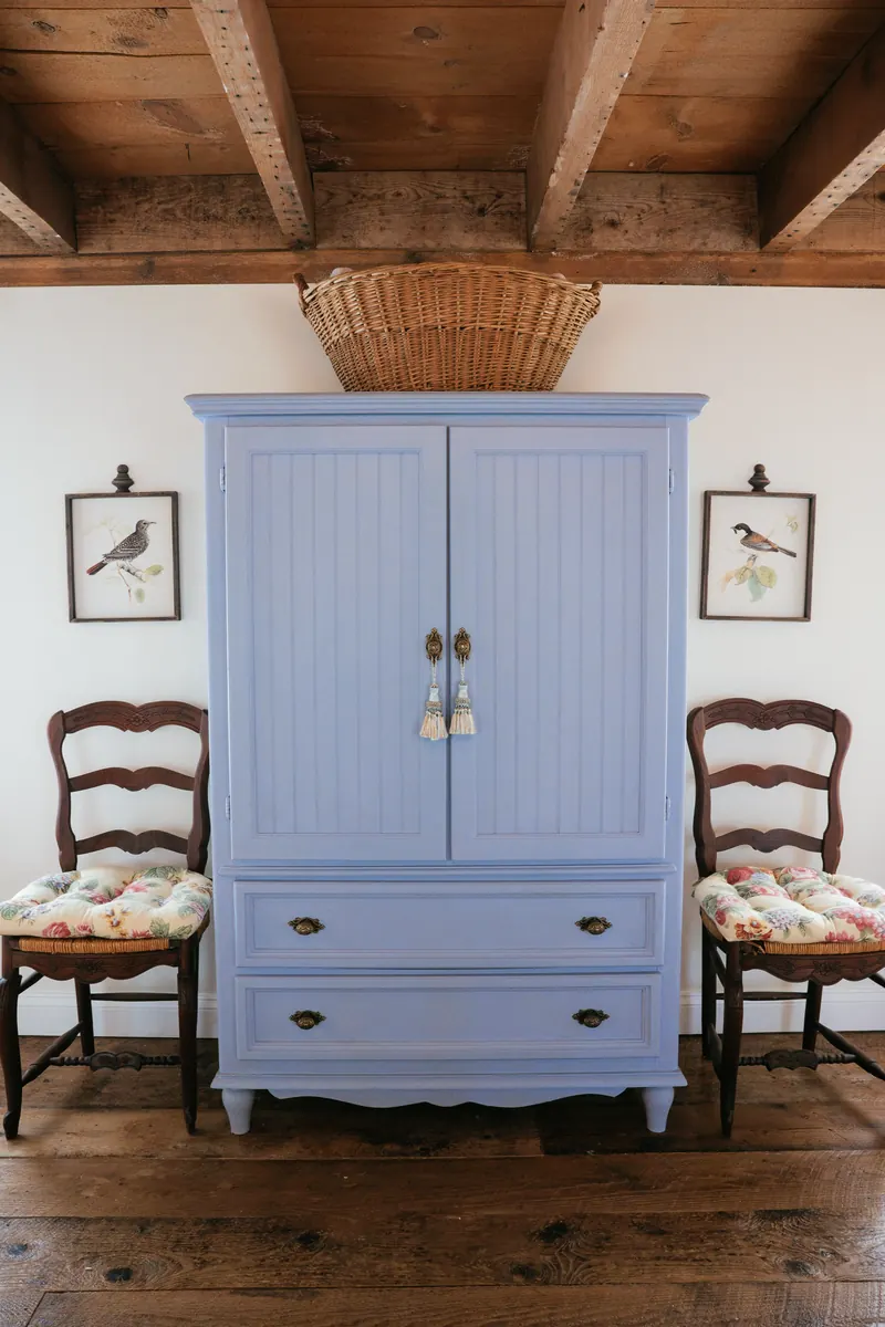 Provence — a blue painted armoire between two rush-seat chairs, under beams.