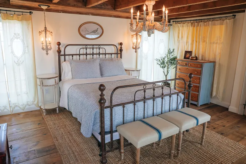 Provence — the iron bed seen head-on under beams, a chandelier above it.