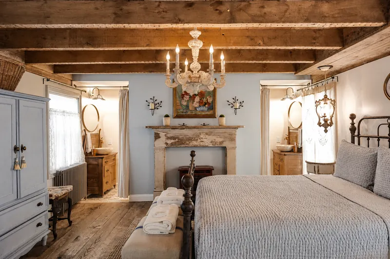 Provence — the bed square on to a stone fireplace, a chandelier centred on the beam above and a washstand framed in each doorway.