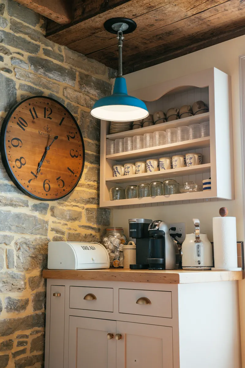 A coffee station beneath a large station clock, against a bare stone wall.