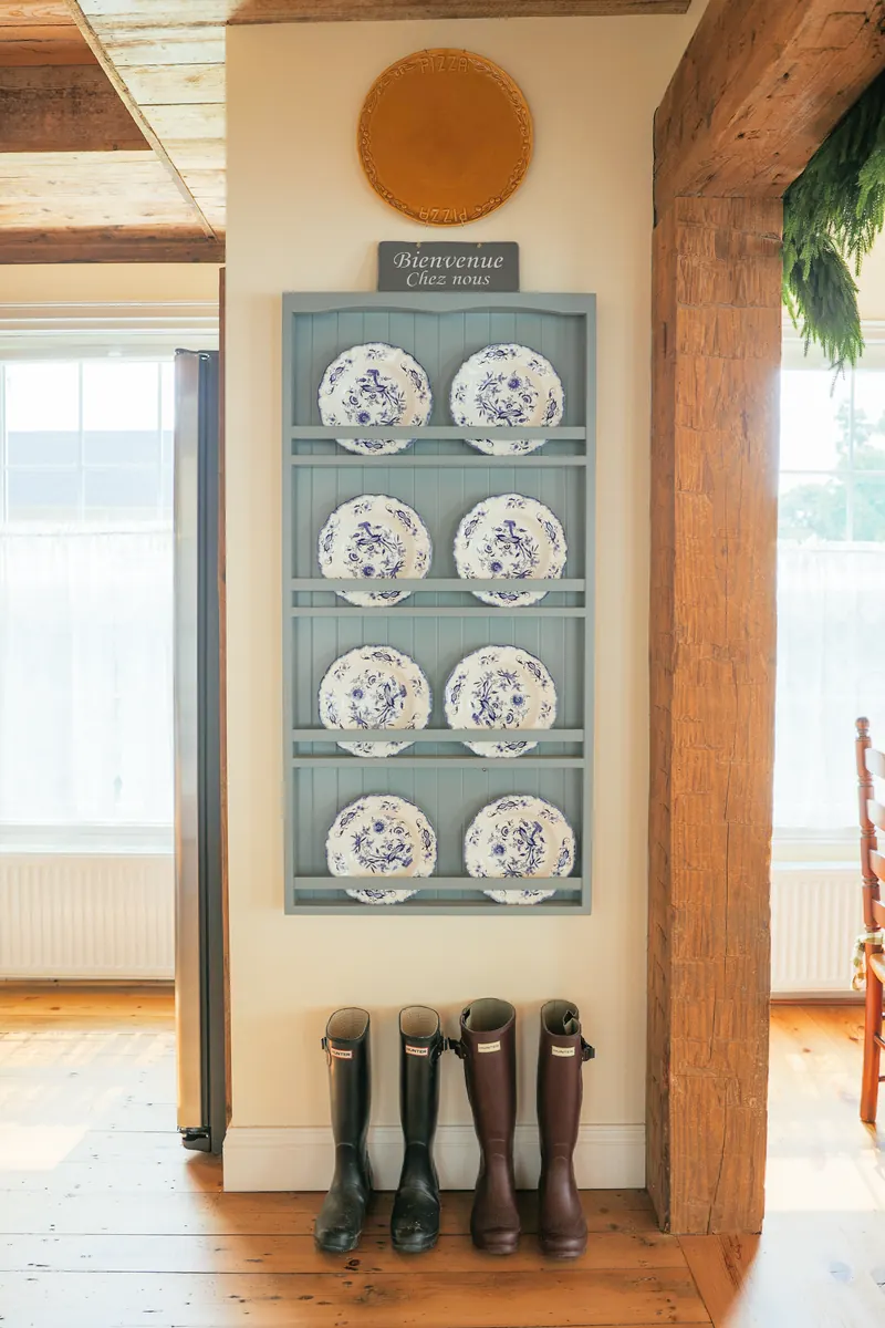 A blue plate rack of transferware plates over a row of wellington boots.