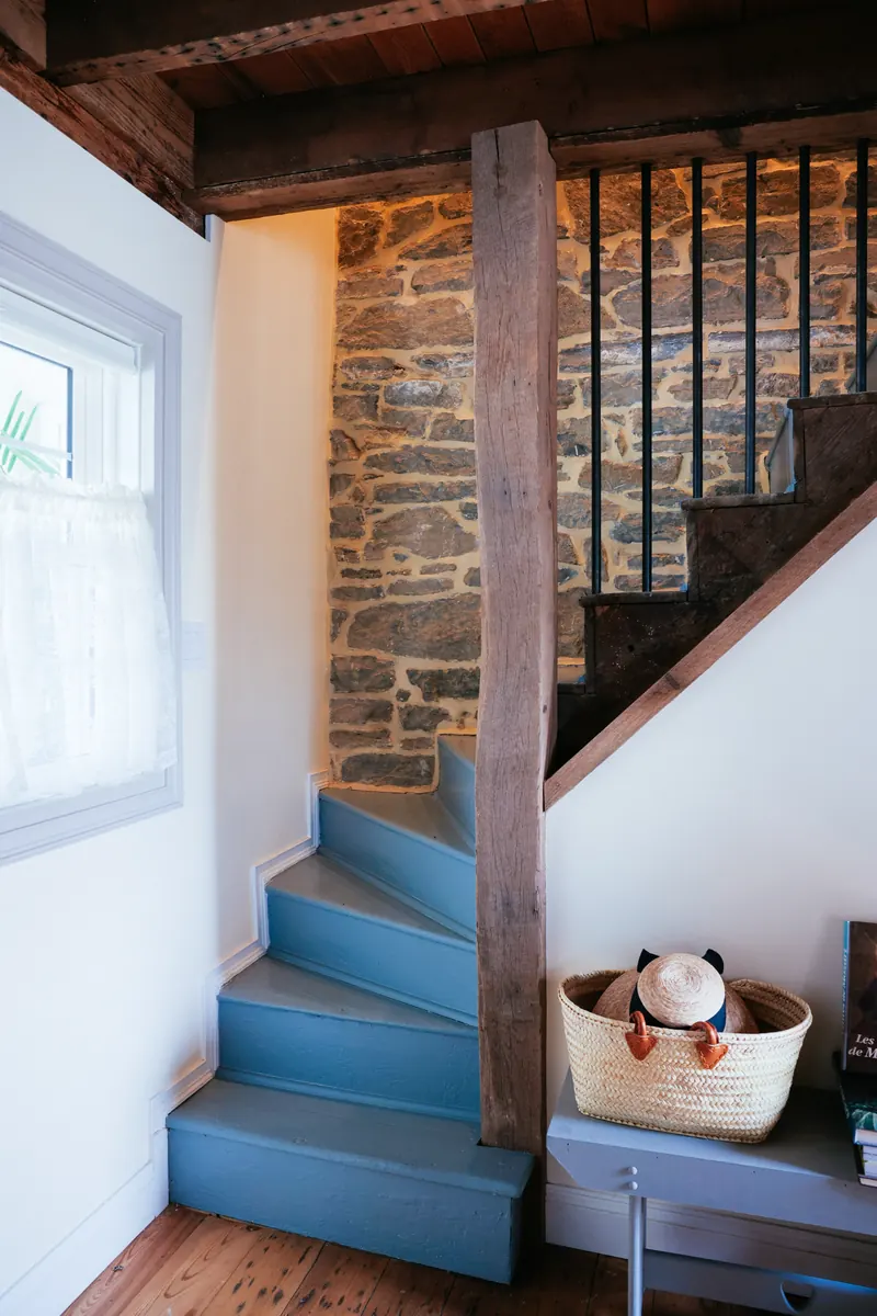 A blue-painted winder stair against bare fieldstone, with an iron balustrade and a market basket at the foot.